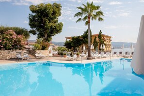 Una piscina con sillas de descanso, palmeras y vistas a un edificio con balcones.