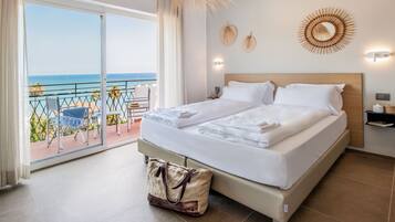 Une chambre d’hôtel avec un lit, une valise et un balcon donnant sur la mer.