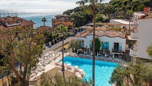 A resort with a swimming pool, lounge chairs, and a view of the sea.