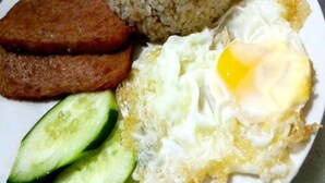Une assiette contenant du riz, un œuf frit, des tranches de concombre et un morceau de viande.