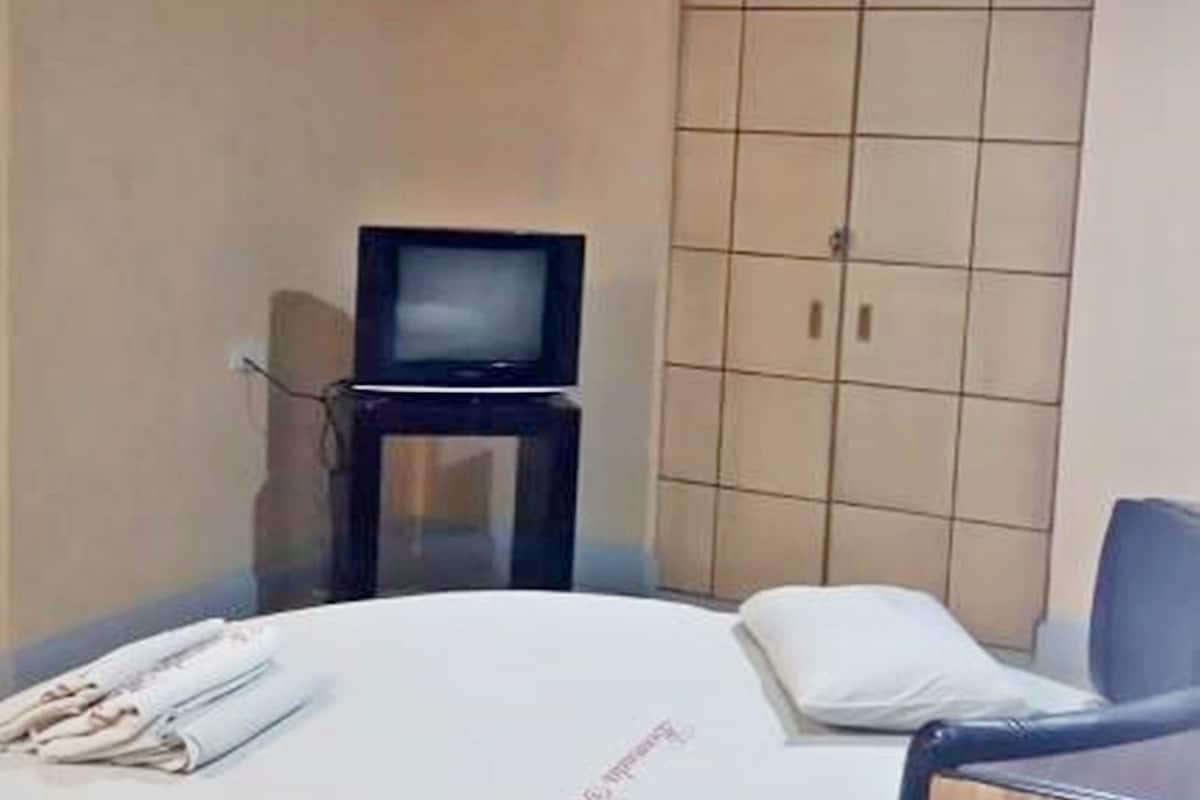 A hotel room with a bed, a television, a wardrobe, and a desk.