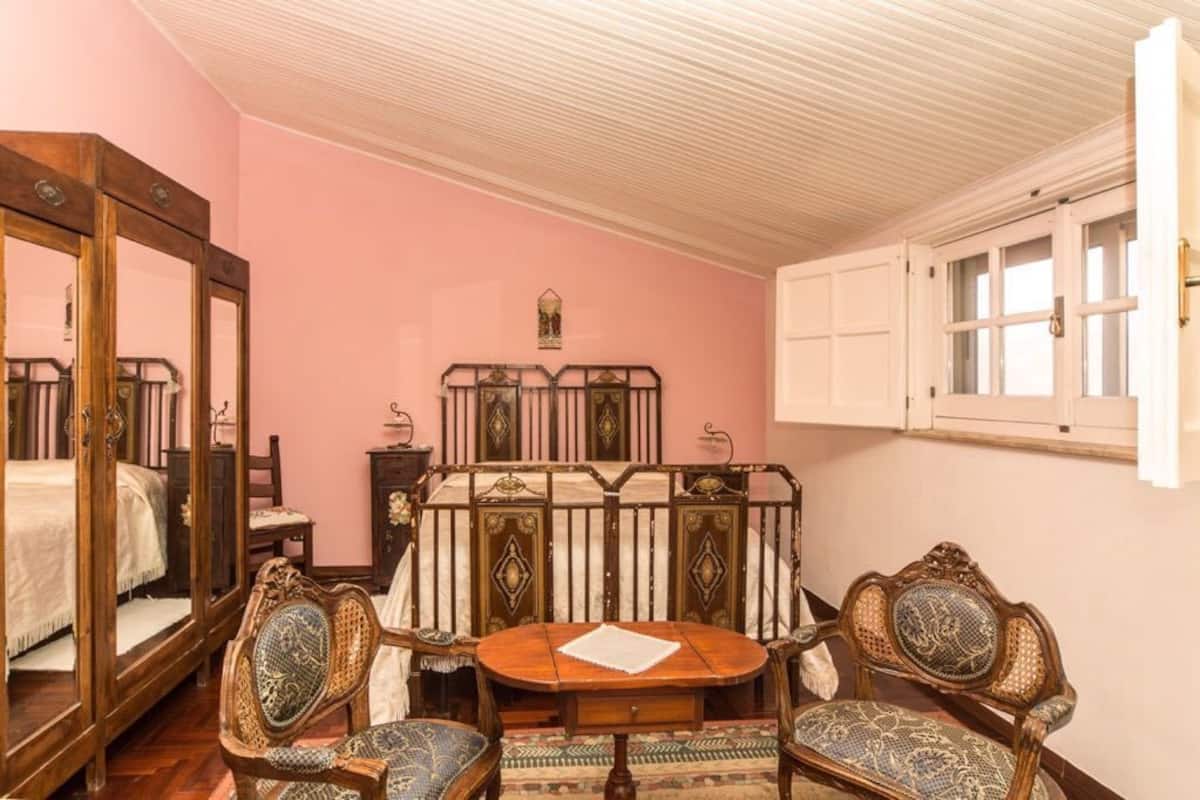 A room with a bed, a wooden chair, a table, and a cabinet.