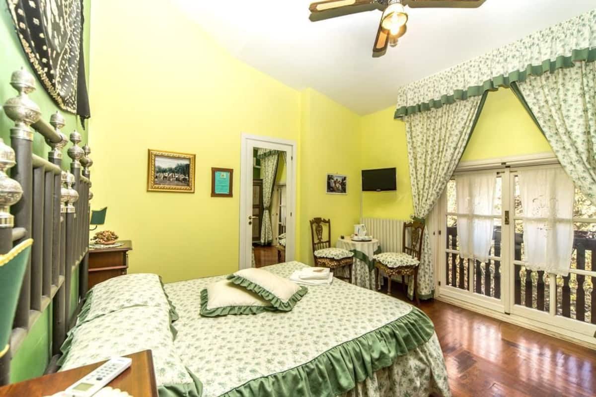 A room with a bed, a desk, a chair, a television, and a window with curtains.