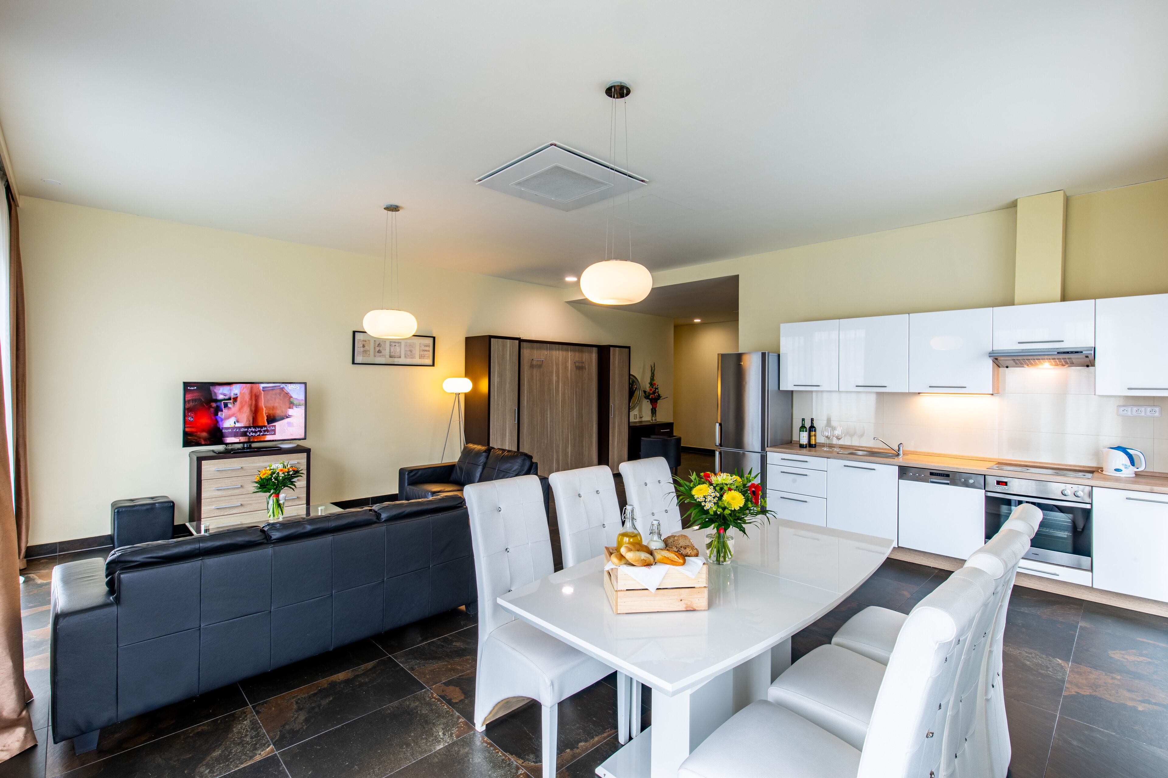 Una sala de estar moderna con sofá, mesa de comedor y sillas. Se observa una zona de cocina con armarios y electrodomésticos.