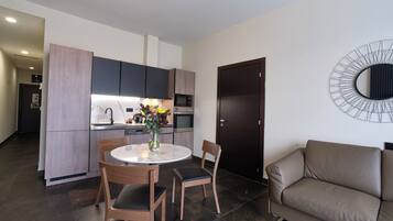 A modern kitchen with dark cabinets, a round dining table, and a sofa in a living area.