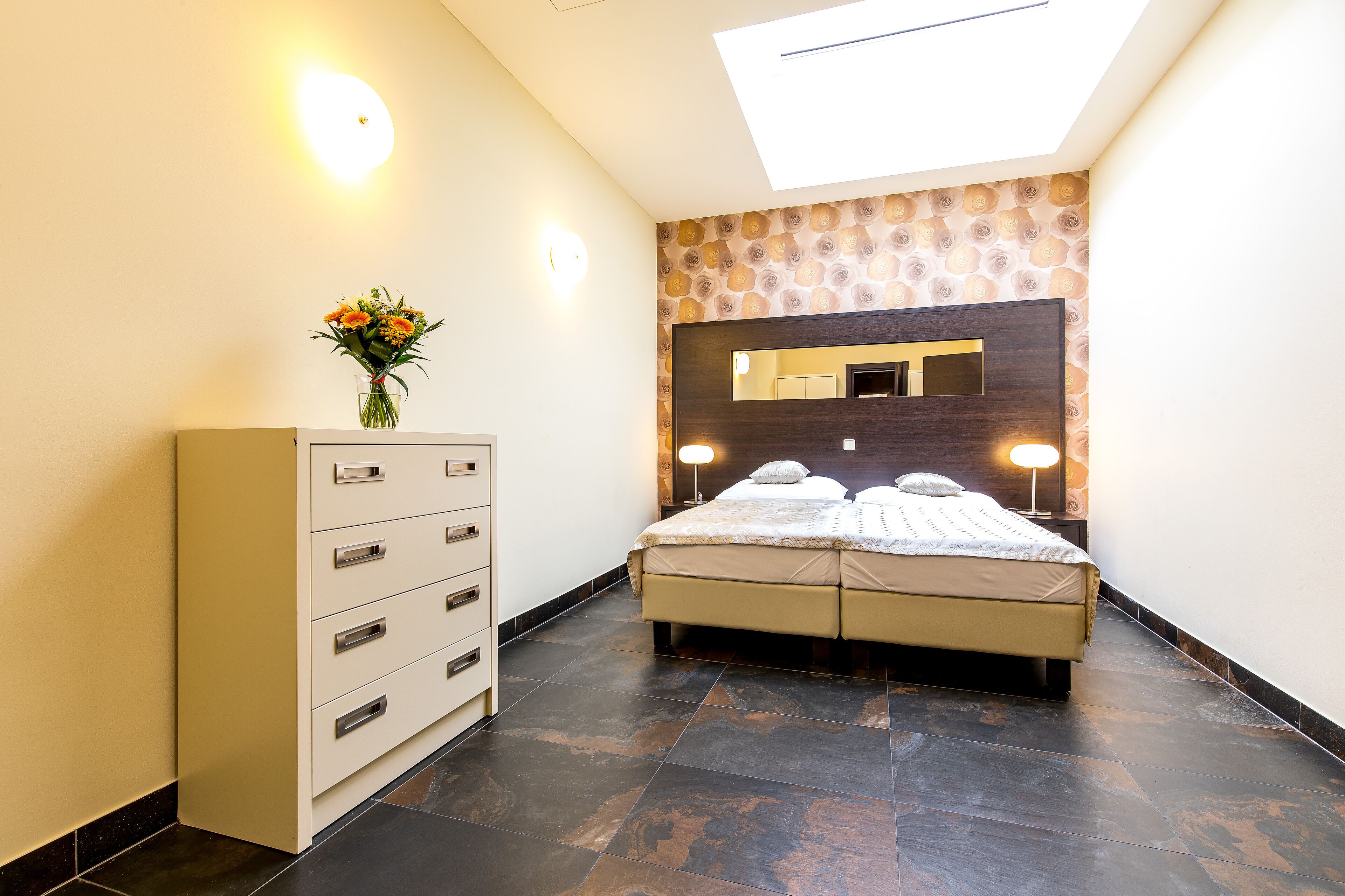 Ein modernes Schlafzimmer mit Dachfenster, einem Nachttisch mit Lampe, einer Kommode und einem Spiegel an der Wand.