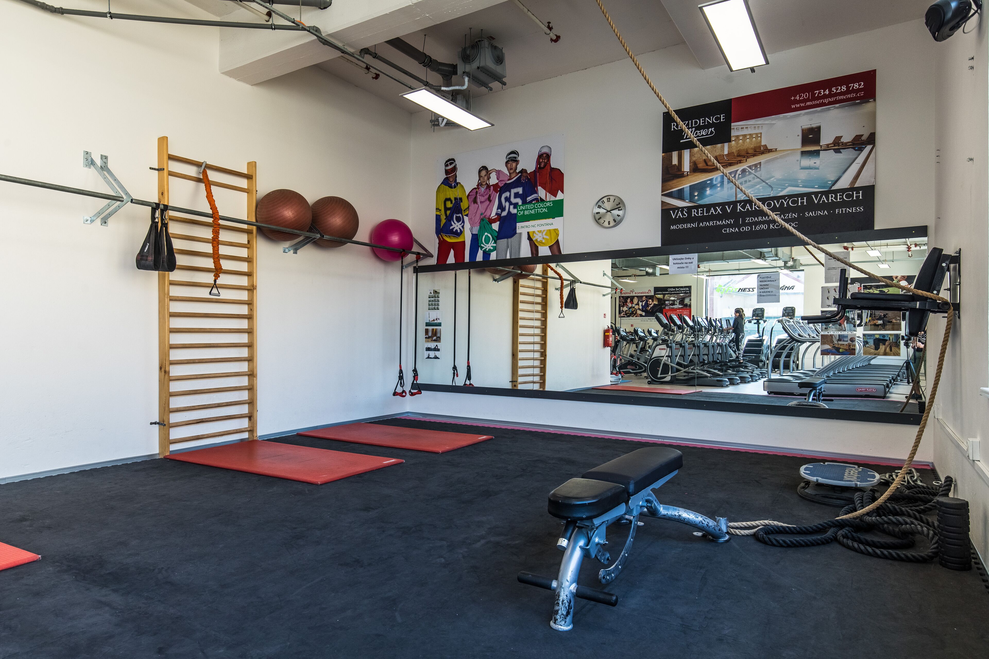 A gym with exercise equipment, a wooden ladder, and a mirror reflecting the room.