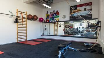 A gym with exercise equipment, a wooden ladder, and a mirror reflecting the room.