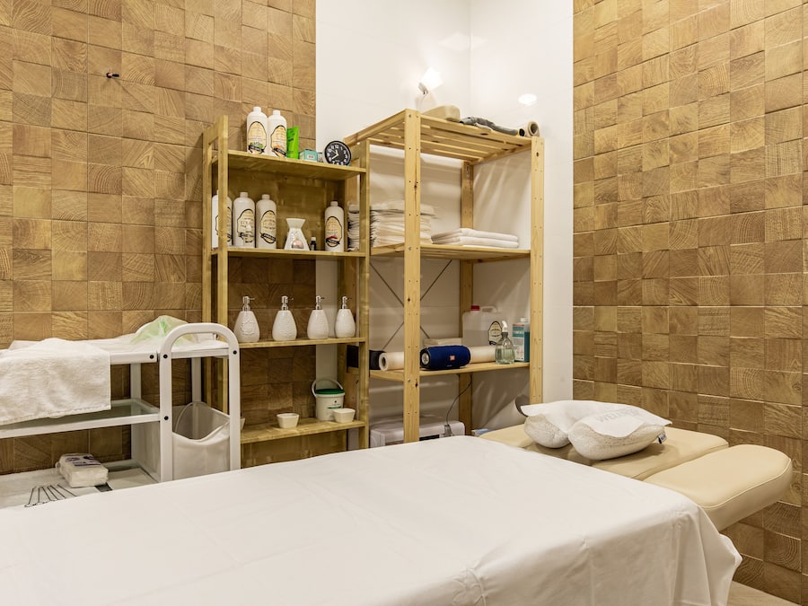 Un baño con paredes de madera, un estante de madera con artículos de aseo, un lavamanos blanco y una bañera blanca.