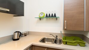 Una cocina con un lavamanos, una tetera, un reloj y un escurreplatos verde.