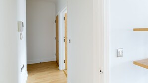 Un pasillo con paredes blancas, piso de madera y una puerta que da a otra habitación.