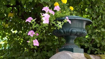 Un bac à fleurs en pierre, surmonté d’un rebord vert, entouré d’un feuillage verdoyant et de fleurs roses.