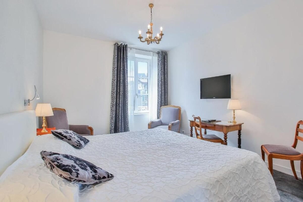 Une chambre d’hôtel avec un grand lit, un bureau avec une chaise, une télévision et un lustre.