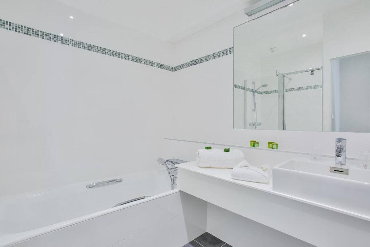 Un baño moderno con un espejo grande, sanitarios blancos y una zona de ducha con azulejos.