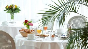 Aamiaispöytä on katettu: siellä on croissantteja, hedelmäkori, maljakko täynnä kukkia, kannu, kuppi, lasi appelsiinimehua ja lautanen, jossa on keitetty kananmuna.