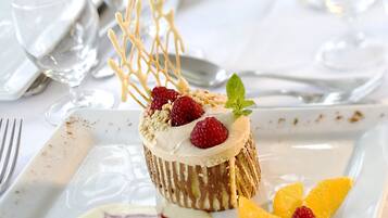 A dessert plate with a cake, strawberries, and a decorative leaf on a white tablecloth.