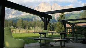 Une terrasse en bois avec une table de pique-nique et des fauteuils en forme de haricot vert, offrant une vue sur un paysage montagneux.