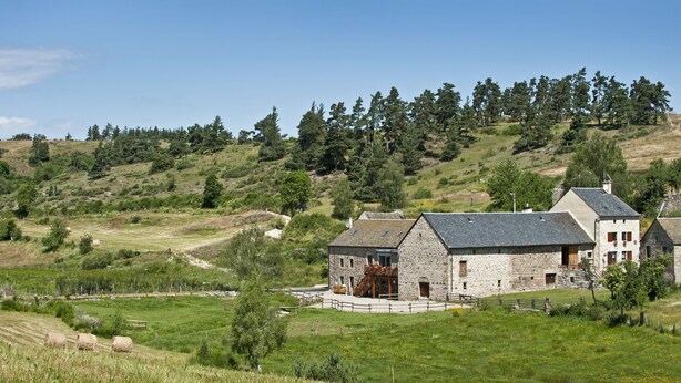 A stone farmhouse with a large barn, surrounded by rolling hills and a clear sky. - Les Granges de Bigose (Rimeize)