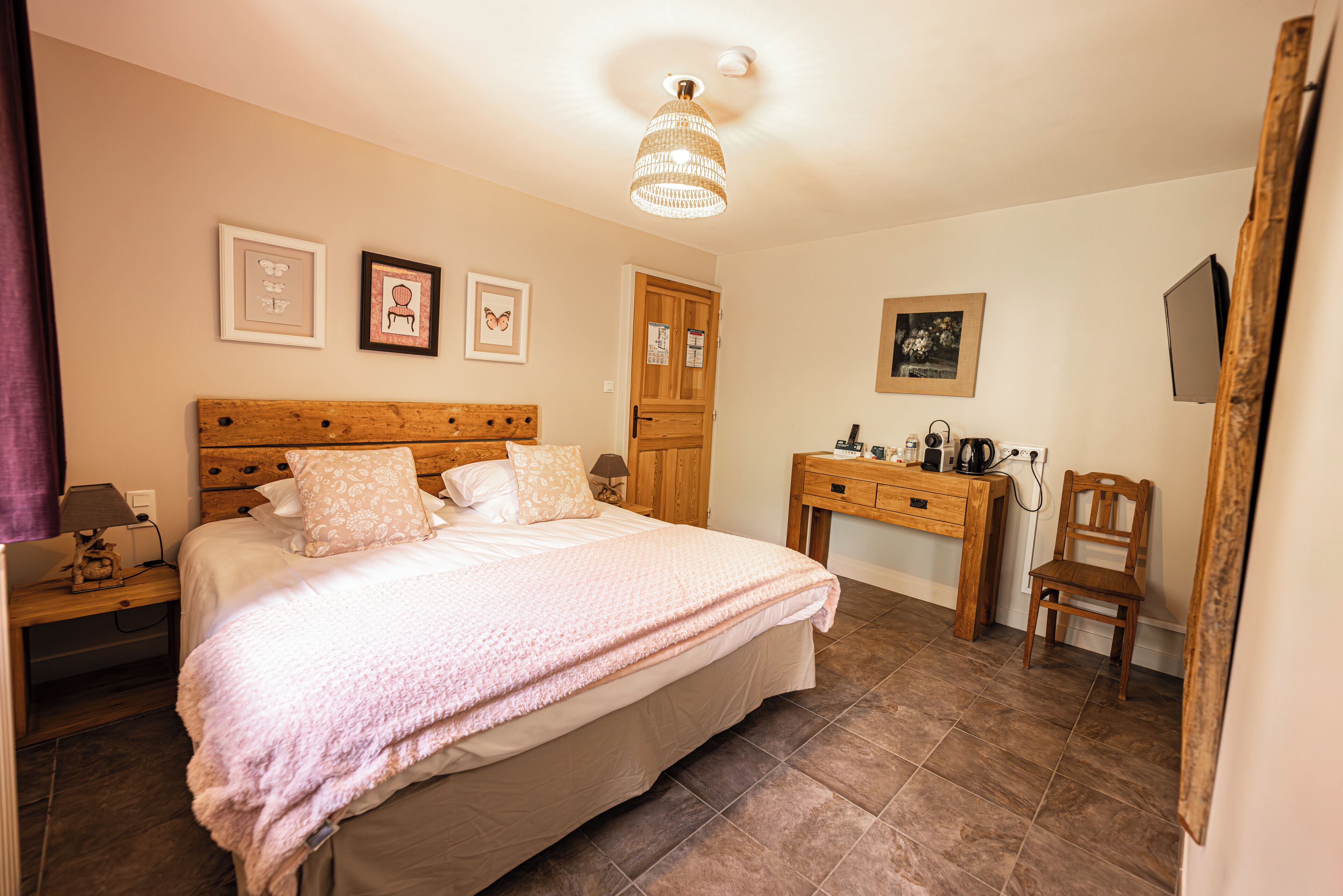 A bedroom with a bed, wooden headboard, bedside table, desk, chair, and a ceiling light fixture.