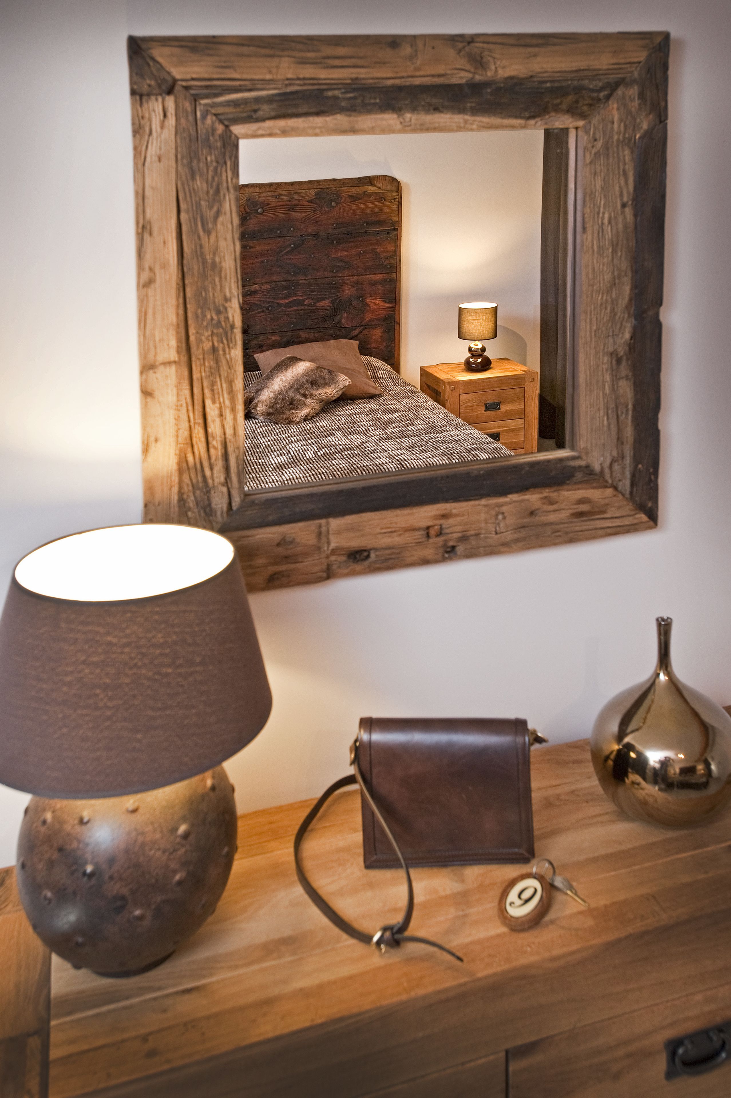 Une table de chevet en bois, avec une lampe, un miroir et une petite horloge.
