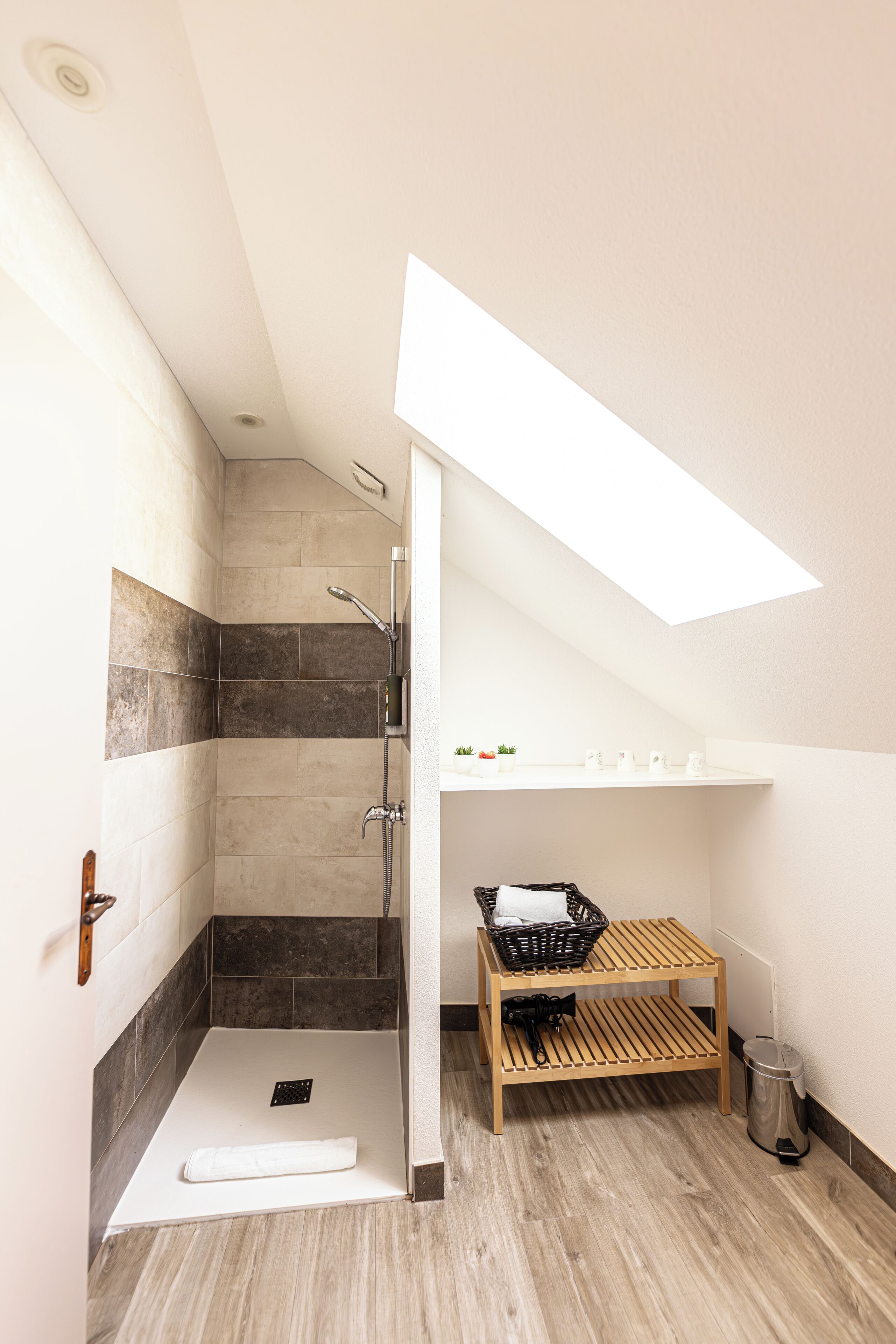 Ein modernes Badezimmer mit Dachfenster, einer Dusche, einer Holzbank und einem kleinen Ablagefach für Toilettenartikel.