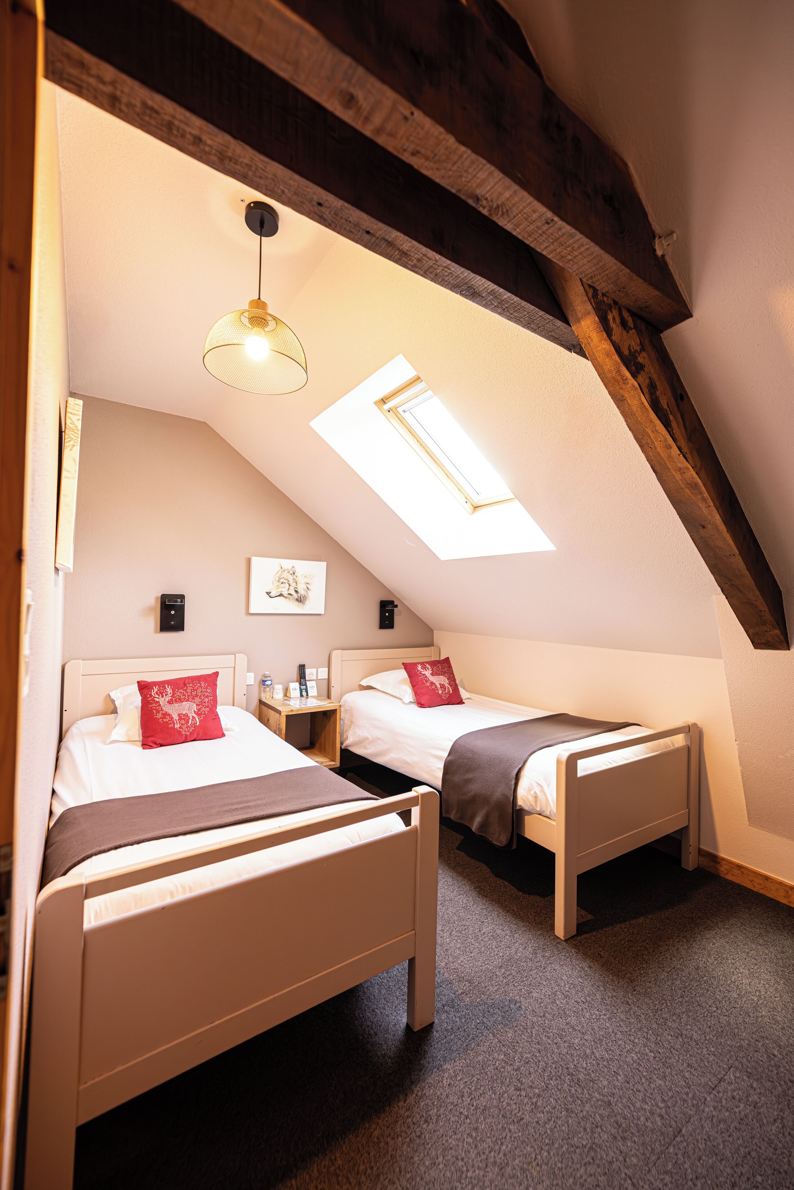 A cozy attic bedroom with two beds, a skylight, and a wooden ceiling beam.