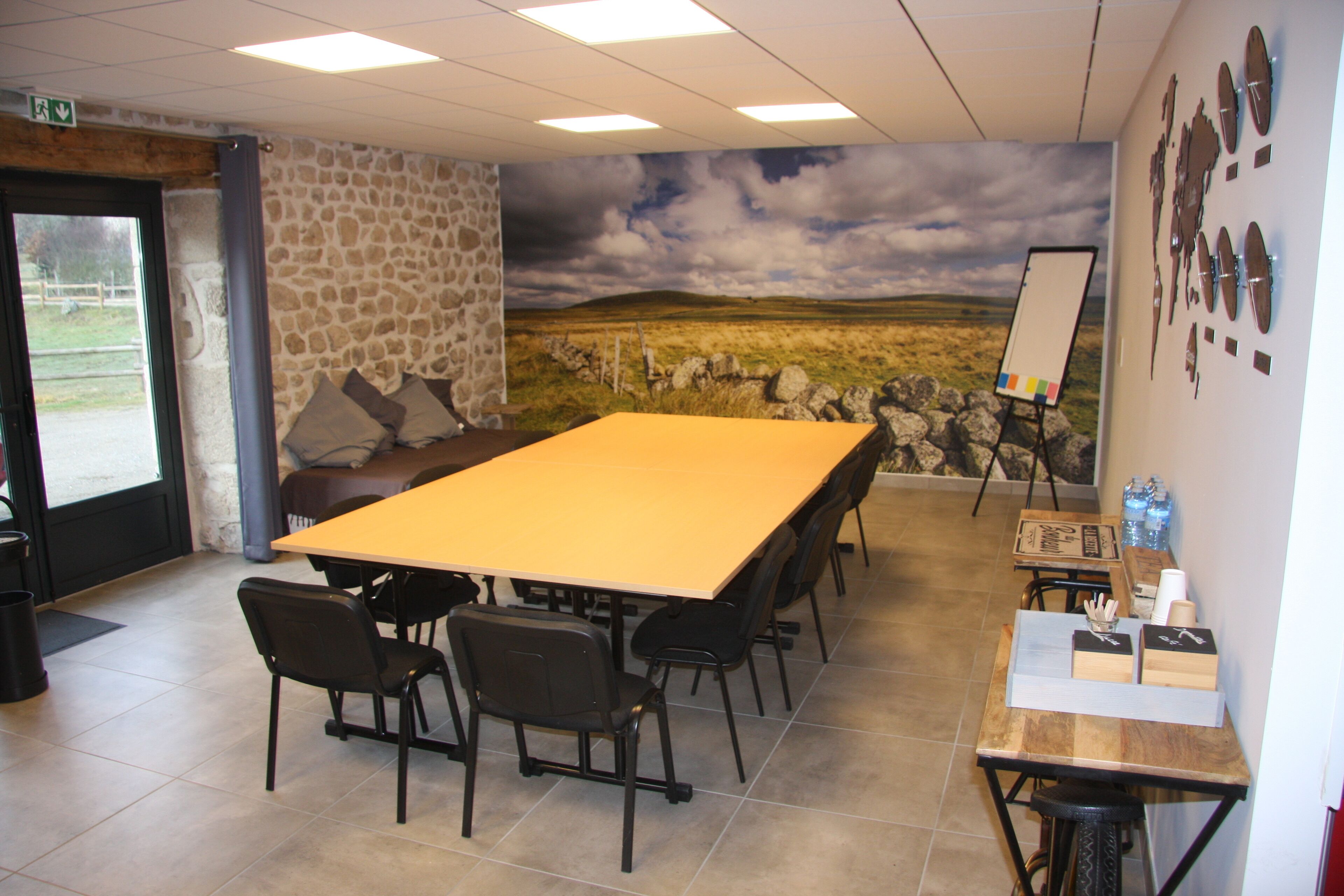Un salón de conferencias con una larga mesa, sillas, una pizarra y un mural de piedra en la pared.