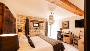 A bedroom with a large bed, wooden beams, stone walls, a desk, and a television. - Les Granges de Bigose (Rimeize)