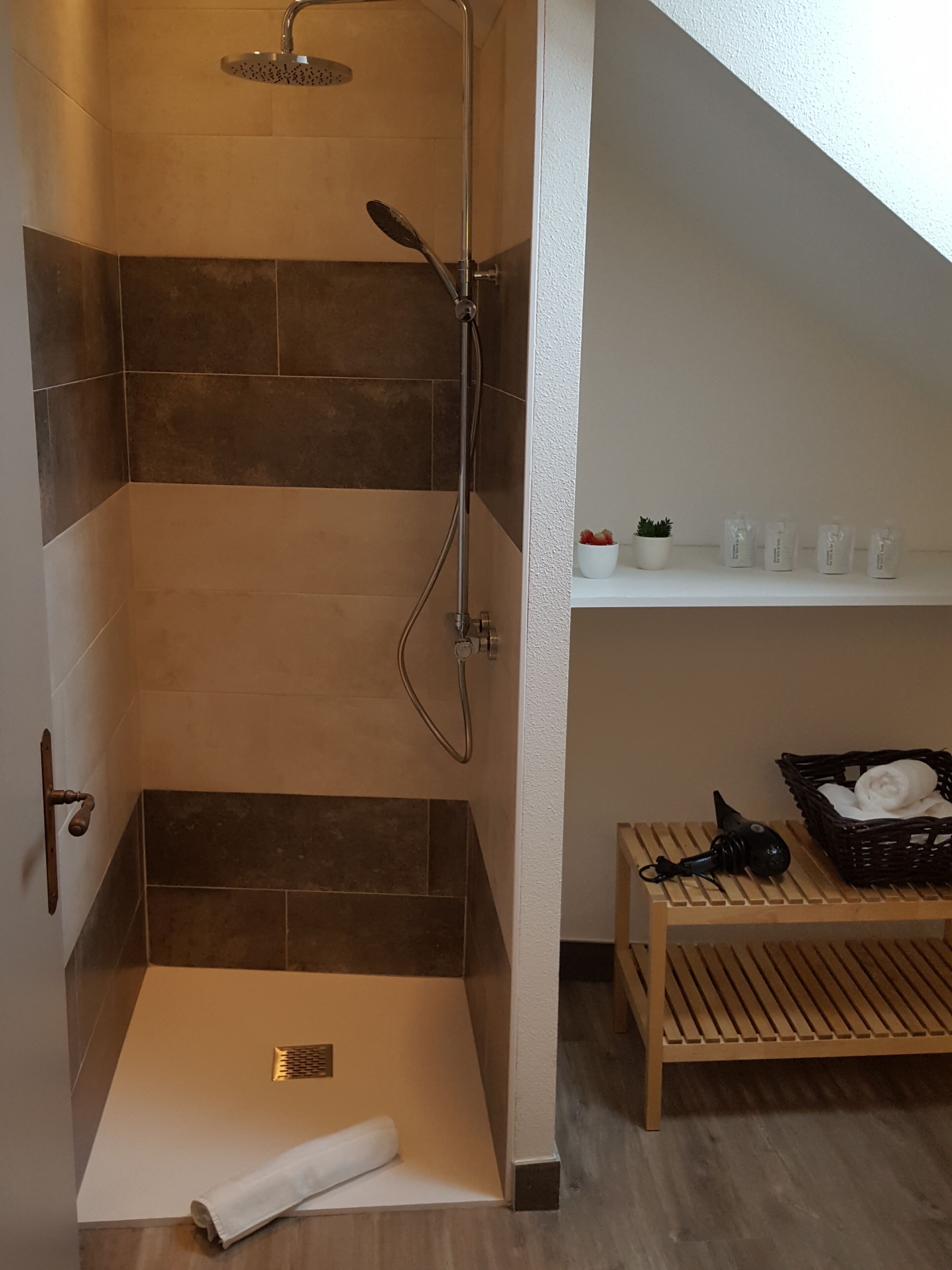 A shower area with a glass door, a wooden bench, and a shelf with toiletries.