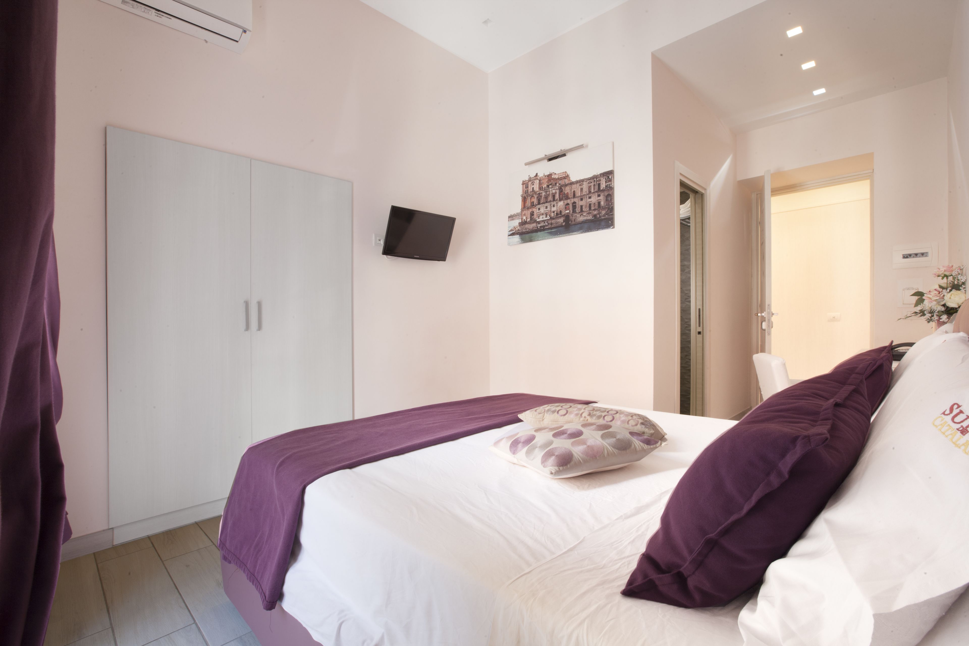 A bedroom with a bed, a wardrobe, a flat-screen TV, and a framed picture on the wall.
