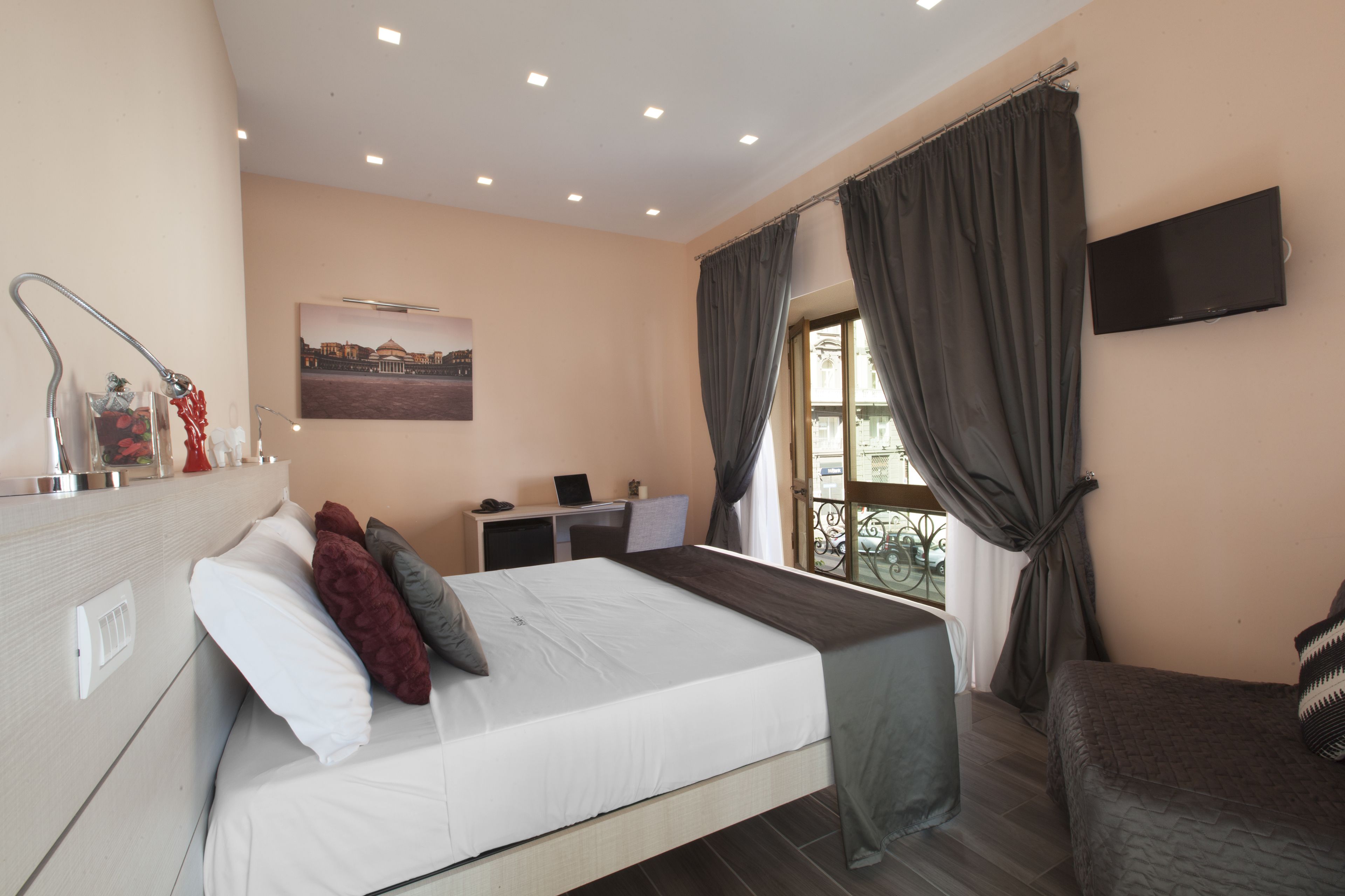 A bedroom with a bed, a desk, a chair, a TV, and a window with curtains.