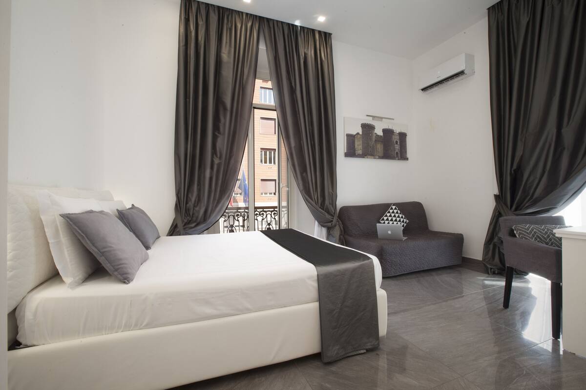 A modern hotel room with a large bed, a sofa, and a desk.