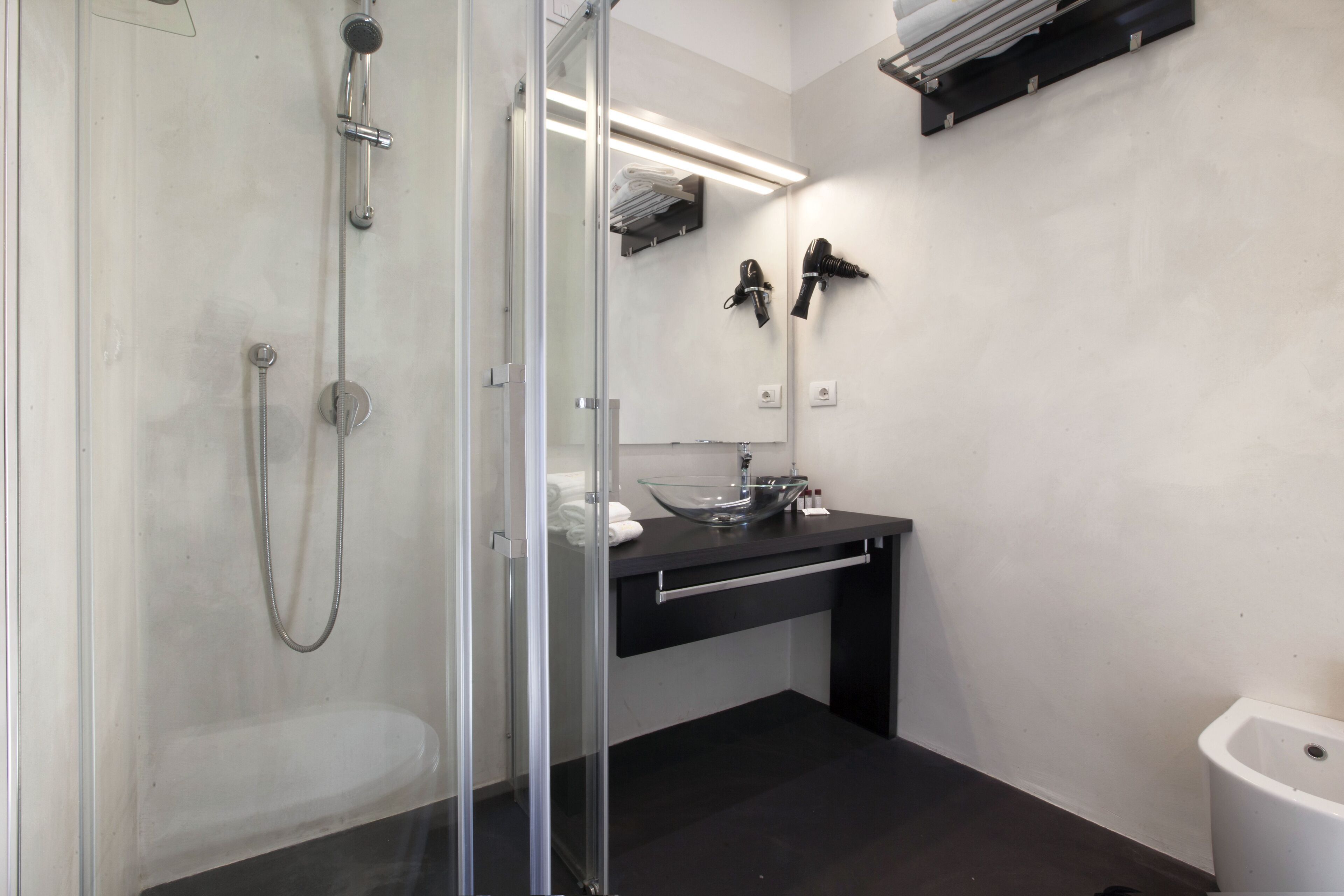 A modern bathroom with a glass-enclosed shower, a black sink, and a white toilet.