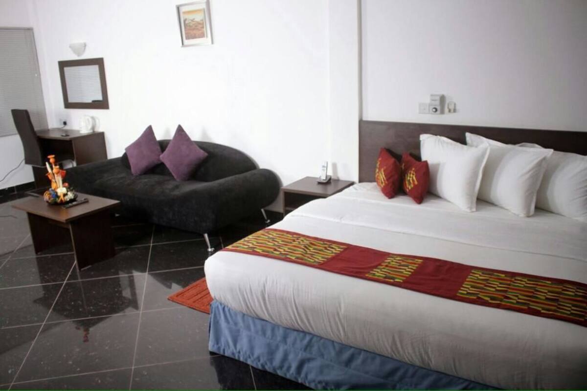 A hotel room with a bed, a desk, a chair, and a small table with a decorative item.