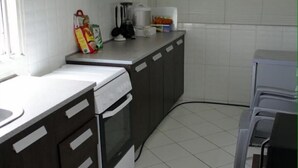A kitchen with dark cabinets, a white countertop, and a stove. - PSB Guest House (Accra)
