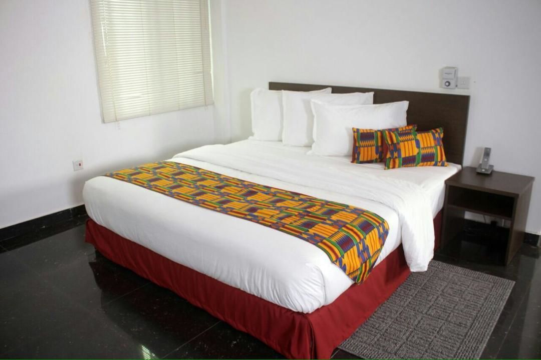 A hotel room with a large bed, white bedding, a colorful throw blanket, and a red skirted bed base.