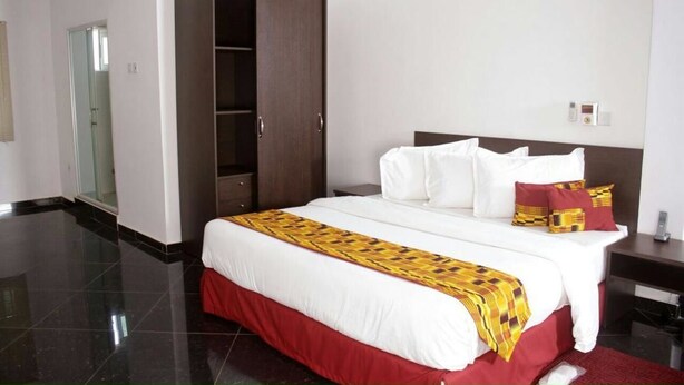 A hotel room with a large bed, a wardrobe, and a bedside table. - PSB Guest House (Accra)