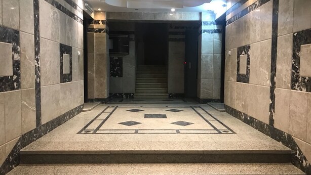 A marble-floored lobby with a geometric tile pattern, a staircase leading to an elevator, and a recessed ceiling light. - Maadi Royal Palace (Cairo)