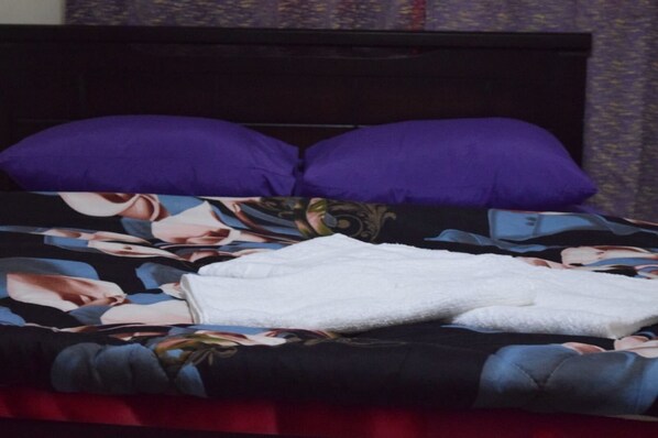 Una cama con una colcha estampada y dos almohadas moradas.