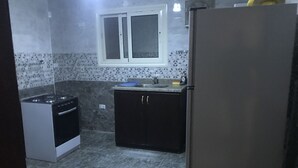 A compact kitchen with a gas stove, a refrigerator, dark cabinets, and a window above the sink. - Maadi Royal Palace (Cairo)
