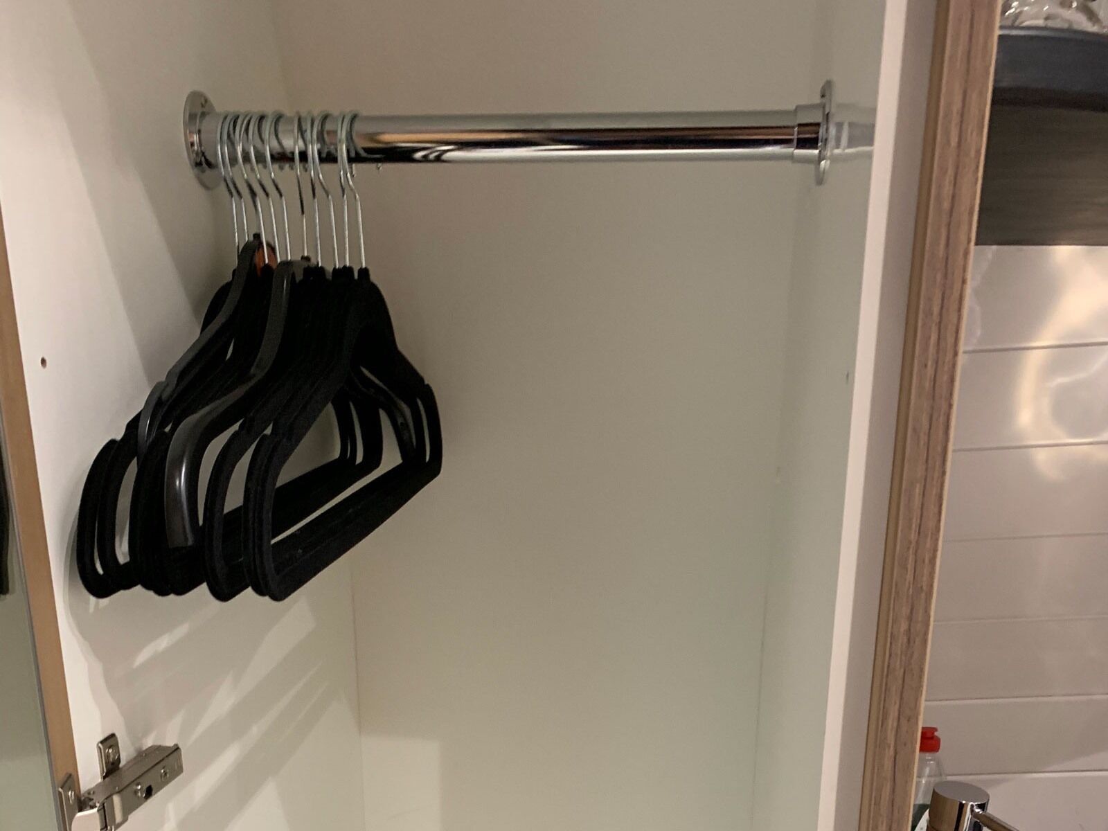 Une salle de bain avec un mur recouvert de carreaux blancs, un porte-serviettes en chrome et une porte dotée d’une poignée argentée.