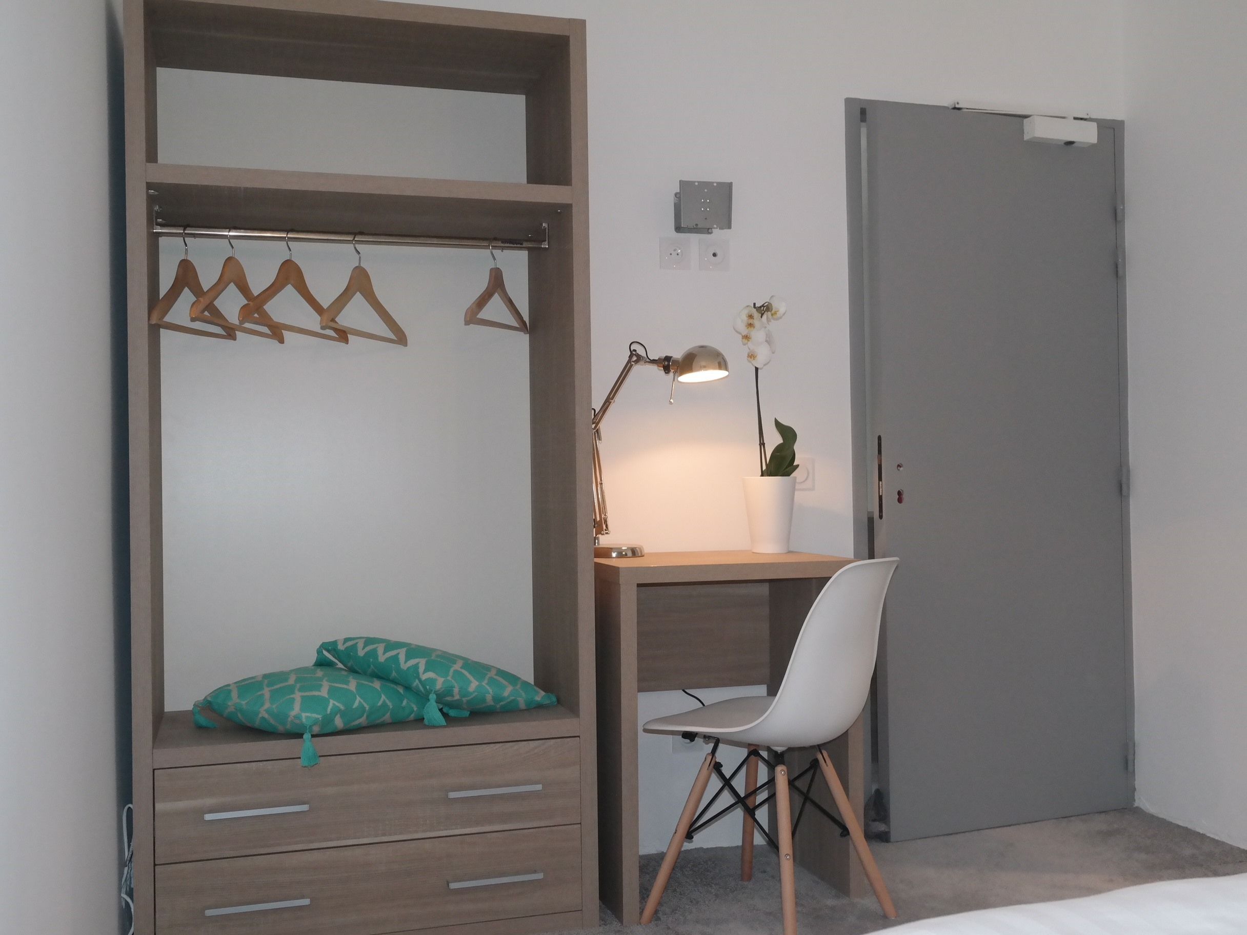 Une chambre à coucher avec un lit, un bureau, une chaise, une lampe suspendue et une porte.