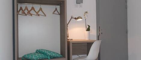 Un dormitorio con cama, escritorio, silla, lámpara colgante y una puerta.