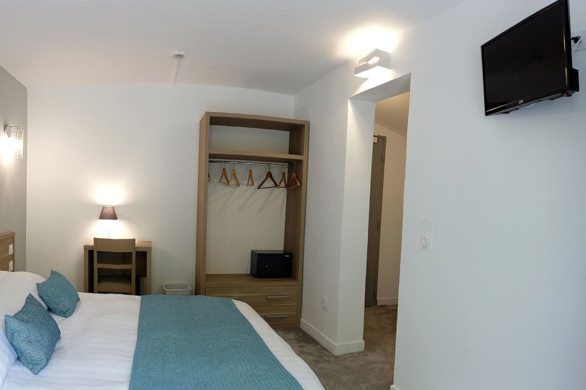 A hotel room with a bed, bedside table, lamp, and a painting on the wall.