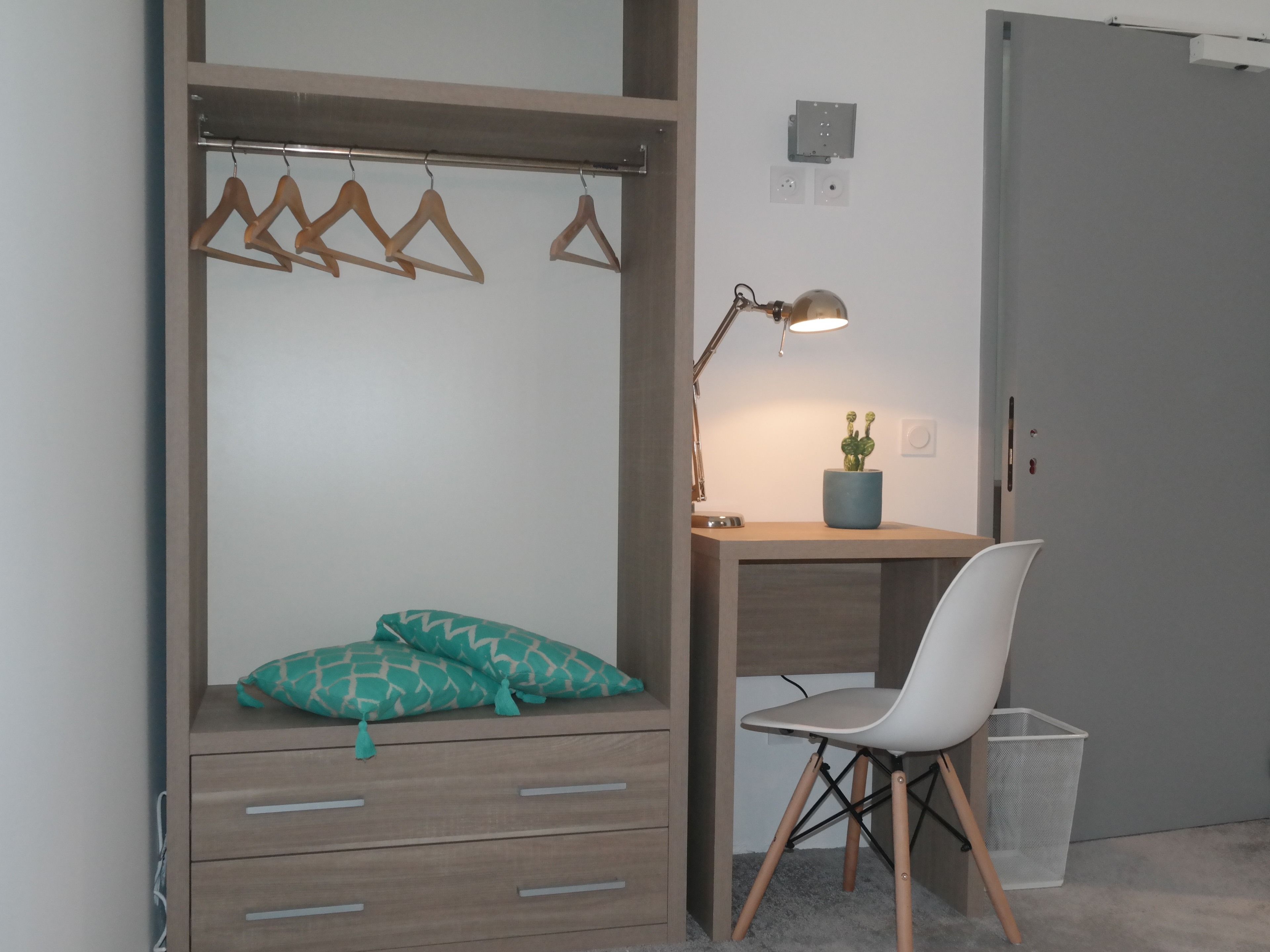 A bedroom with a bed, a desk, a chair, a lamp, and a small plant.
