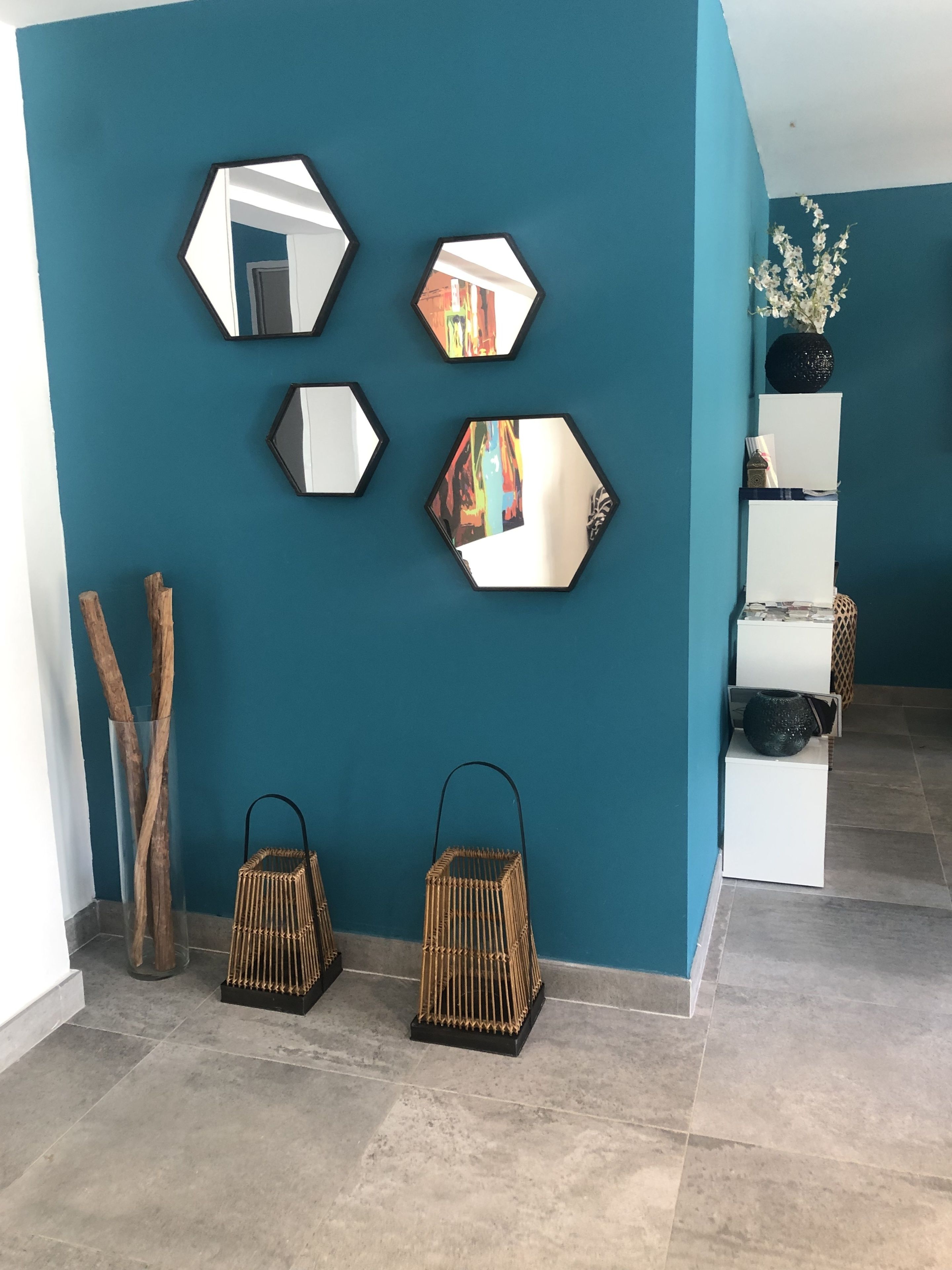 Quarto com paredes verde-água, um balcão de recepção branco e um espelho com reflexo colorido.