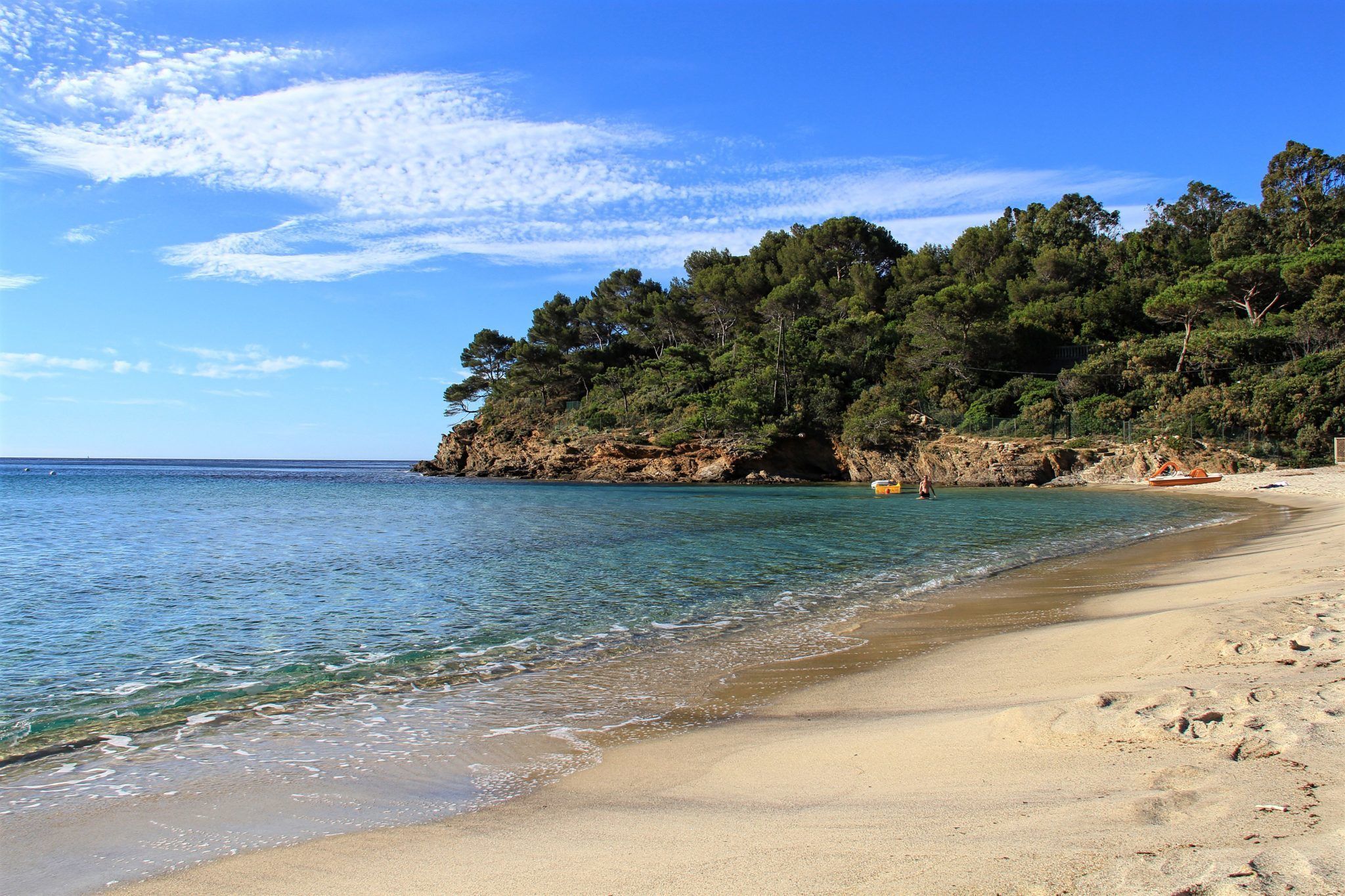 Ein Strand mit klarem Wasser, sandigem Ufer und einer bewaldeten Klippe.