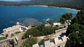 A coastal view with a historical building, clear blue sea, and a beach.
