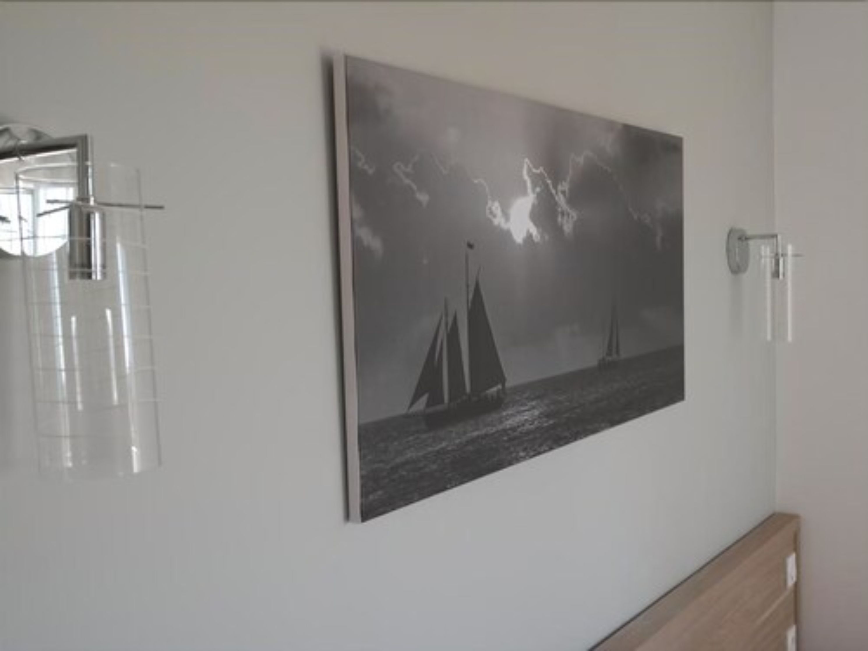 Una habitación con un cuadro grande en blanco y negro de veleros en la pared, un armario de madera y un box de ducha de vidrio.