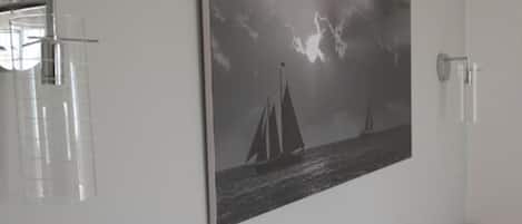 Een kamer met een groot zwart-wit schilderij van zeilboten aan de muur, een houten kast en een douchecabine met glazen wanden.